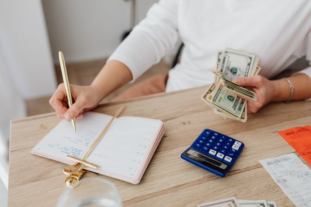 holding cash and writing in planner while using a calculator