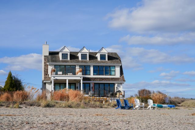 beachfront house with patio chairs surrounded by sand and grasses